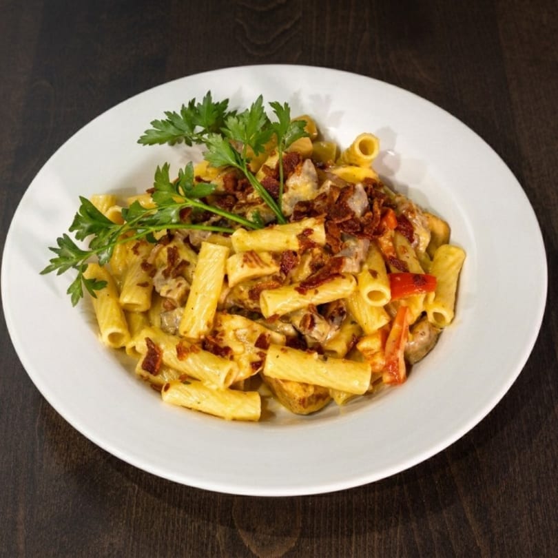 Rigatoni pasta with creamy sauce, bacon bits, red peppers, and parsley on a white plate.