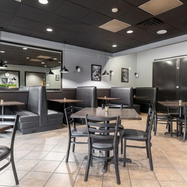 Empty restaurant dining room with black booths, dark tables, and chairs on tiled floor.