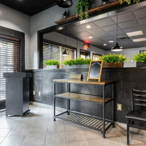 Restaurant interior with dark walls, a wooden console table, and green plants in window boxes.